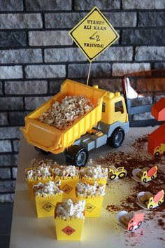 a table topped with yellow cups filled with food next to a construction truck and sign