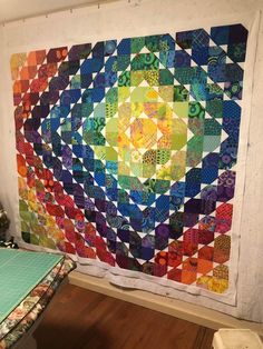 a colorful quilt hanging on the wall next to a wooden table with a bed in front of it