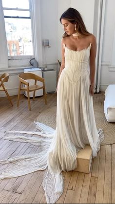 a woman in a white dress standing on a wooden floor next to a chair and window