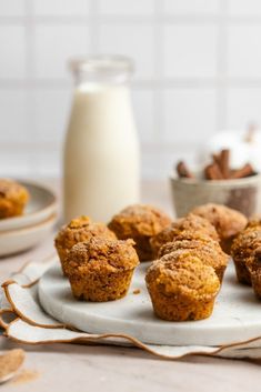 several muffins on a plate next to a glass of milk and bowl of nuts