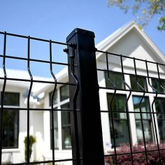 a house behind a metal fence with flowers in the foreground