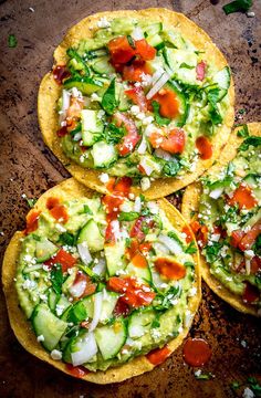 three tortillas with cucumbers, tomatoes and other toppings on a wooden surface