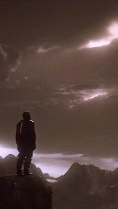 a man standing on top of a mountain under a cloudy sky