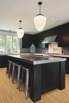 a large kitchen with black cabinets and wooden flooring, along with bar stools