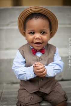 a young boy wearing a brown hat and bow tie sitting on steps with his hands clasped