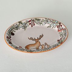 an oval dish with deer and flowers painted on the side, sitting on a white surface