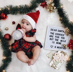 a baby wearing a santa hat and drinking milk from a bottle while surrounded by christmas decorations