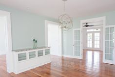 an empty living room with hard wood flooring and white trim on the doors, chandelier, and windows