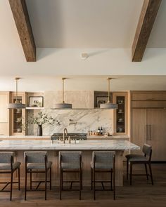 a kitchen with marble counter tops and wooden beams on the ceiling, along with four bar stools