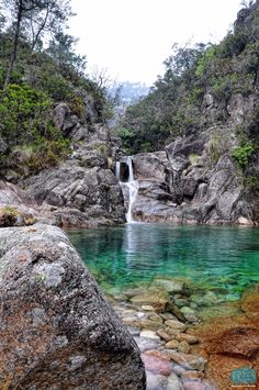 there is a waterfall in the middle of some rocks and green water on the other side