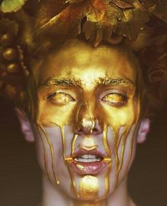 a woman with gold paint on her face and leaves all over her head, covered in chocolate