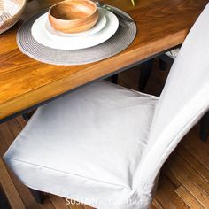 a wooden table topped with a white plate and bowl next to a vase filled with flowers