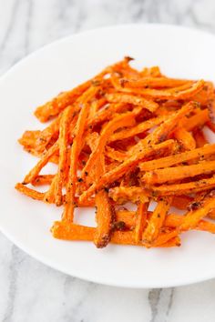 a white plate topped with cooked carrots on top of a marble countertop next to a knife and fork