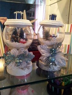 two glass vases with christmas decorations on them sitting on top of a table in front of a mirror