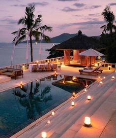 an outdoor swimming pool with candles lit up in front of the water and palm trees