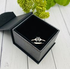 an open ring box sitting on top of a white wooden floor next to green flowers