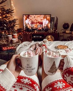 two people holding mugs with hot chocolate on them in front of a christmas tree