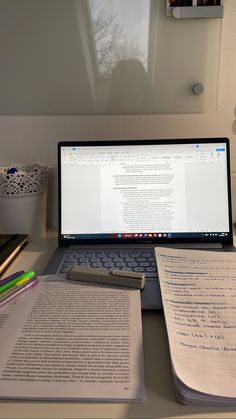 a laptop computer sitting on top of a desk next to an open book and paper