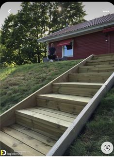 a man standing on top of a green hillside next to a wooden staircase leading up to a red building