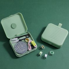 an open green case with sewing supplies in it on a table next to other items