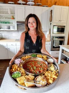 a woman holding a platter full of food in her kitchen with the lid open