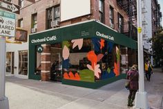 a woman walking down the sidewalk in front of a restaurant called chobani cafe