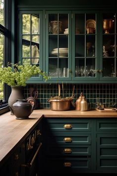 a kitchen with green cabinets and brass pots on the countertop, potted plant next to it