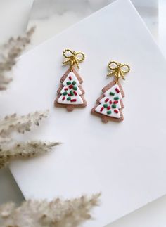 two christmas tree shaped earrings sitting on top of a piece of paper next to some plants