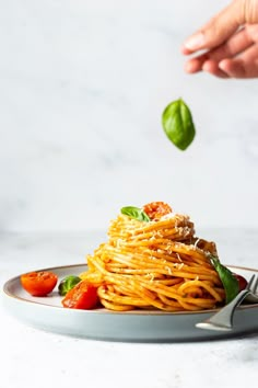 someone is sprinkling basil over spaghetti on a plate