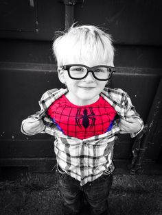 a young boy wearing glasses and a spiderman shirt with his hands on his hips