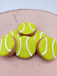 four green cookies with white icing on top of a wooden sliced tree stump