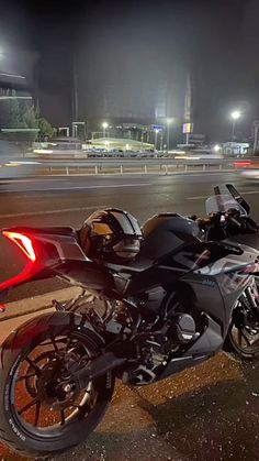 a black motorcycle parked on the side of a road at night with traffic lights in the background