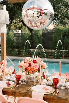 the table is set with plates, silverware and pink flowers in front of an outdoor pool