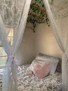 a bed with white curtains and pink heart shaped pillow