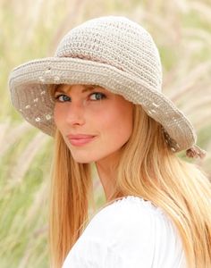 a woman with long blonde hair wearing a white hat and posing in front of tall grass