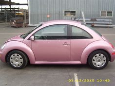 a small pink car parked in a parking lot next to a building with metal structures