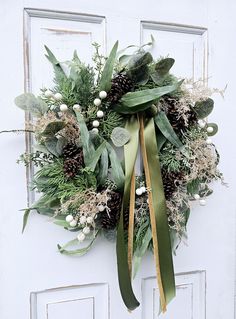 a wreath with pine cones and greenery hangs on the front door