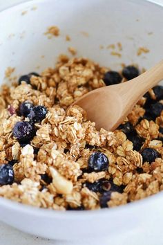 a white bowl filled with granola and blueberries next to a wooden utensil