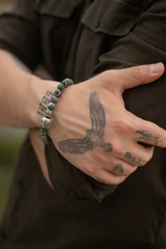 a man with tattoos on his arm and wrist is holding onto a green beaded bracelet