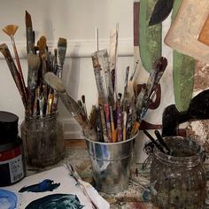 an assortment of paint brushes in a bucket on a table next to other art supplies