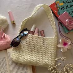 an open book and sunglasses on top of a table next to a knitted bag