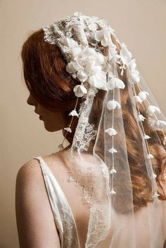 the back of a woman wearing a veil with white flowers on it's head