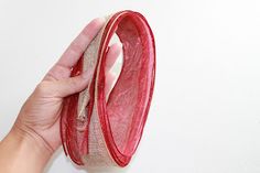 a hand holding a red piece of cloth in front of a white wall and floor