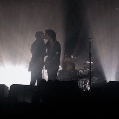 two people standing in front of a stage with their arms around each other as they kiss