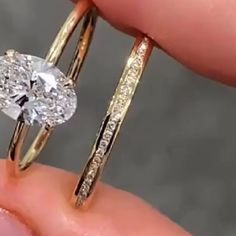 a close up of a person's hand holding two rings with a diamond in the middle