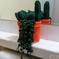 two crocheted cactus planters sitting on top of a white counter next to a mirror