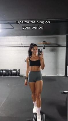 a woman taking a selfie with her cell phone in a gym room while wearing shorts and socks