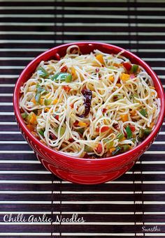 a red bowl filled with noodles and vegetables sitting on top of a metal table cloth