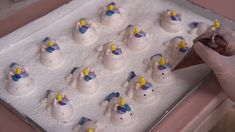 someone is decorating small white snowmen with yellow and blue frosting on them