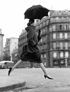 a woman is jumping in the air with an umbrella over her head while wearing high heels